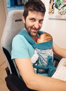 Dad working at desk while baby sleeps in Asteraki mei tai