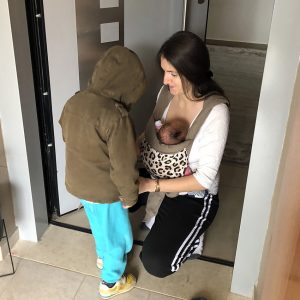 Mom with two kids, wearing the baby and helping the older sibling
