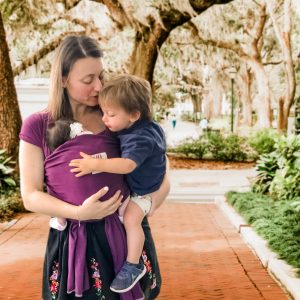Newborn and older sibling held in their mother's arms using an Asteraki wrap